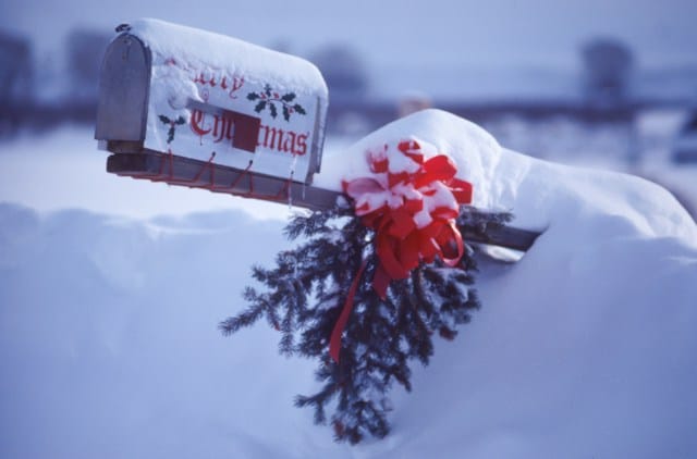 Ein weihnachtlich geschmückter Briefkasten, der aus dem Schnee ragt.