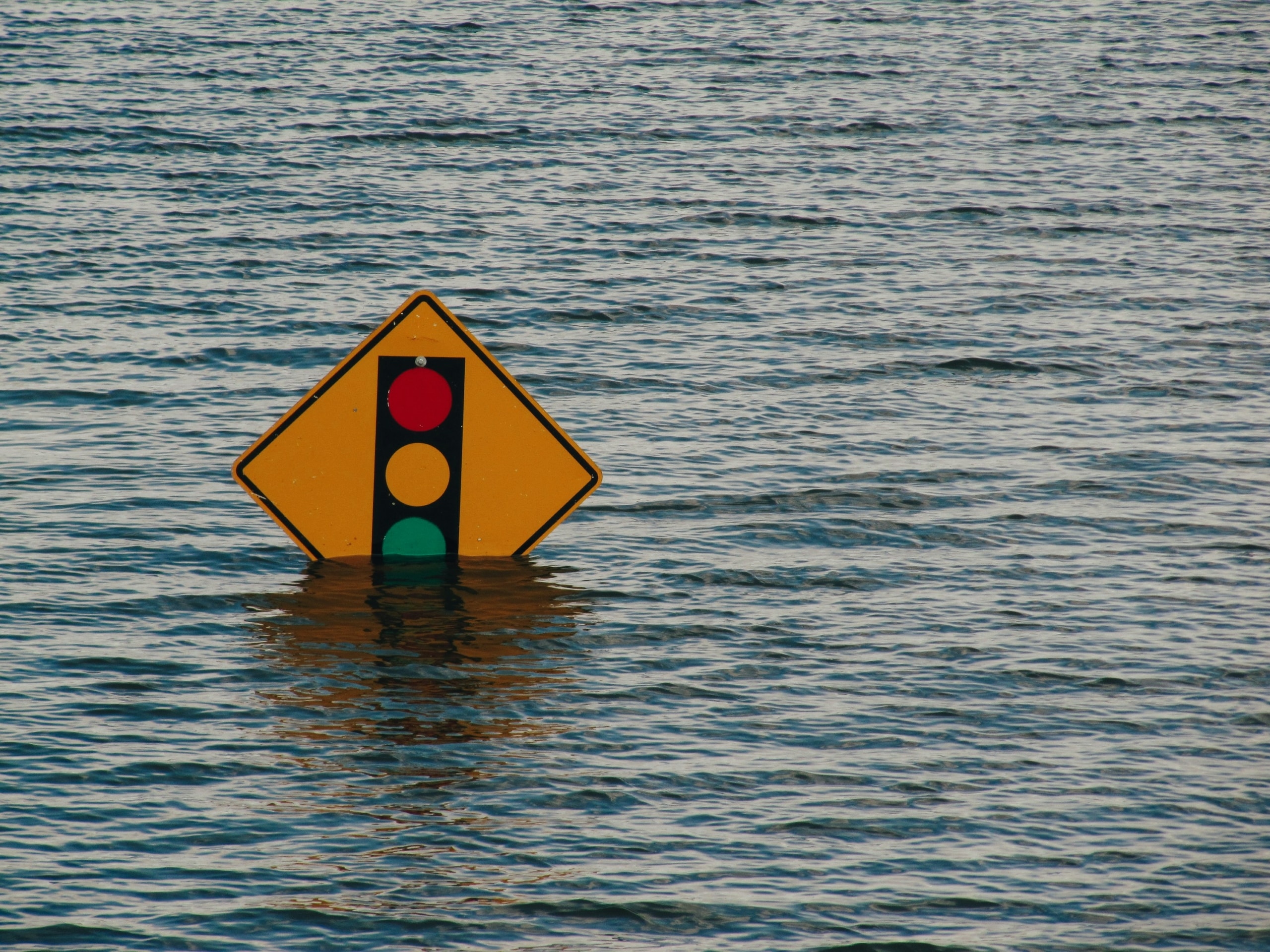 Symbolbild Klimawandel-Folgen: Ein Verkehrsschild, das eine Ampel darstellt, versinkt bei einer Überschwemmung im Wasser.